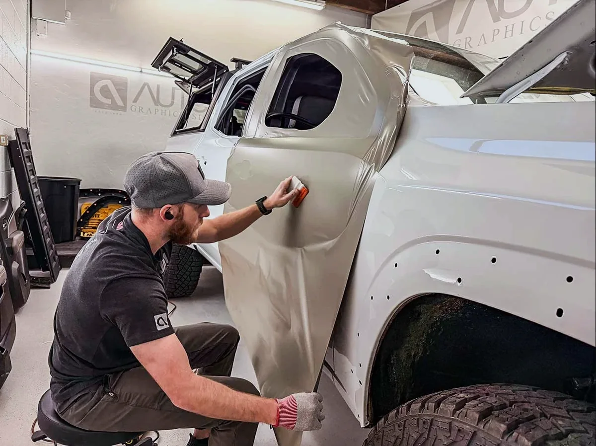 An Auto Trim Plus installer smoothing wrap film onto a truck fender in the shop bay