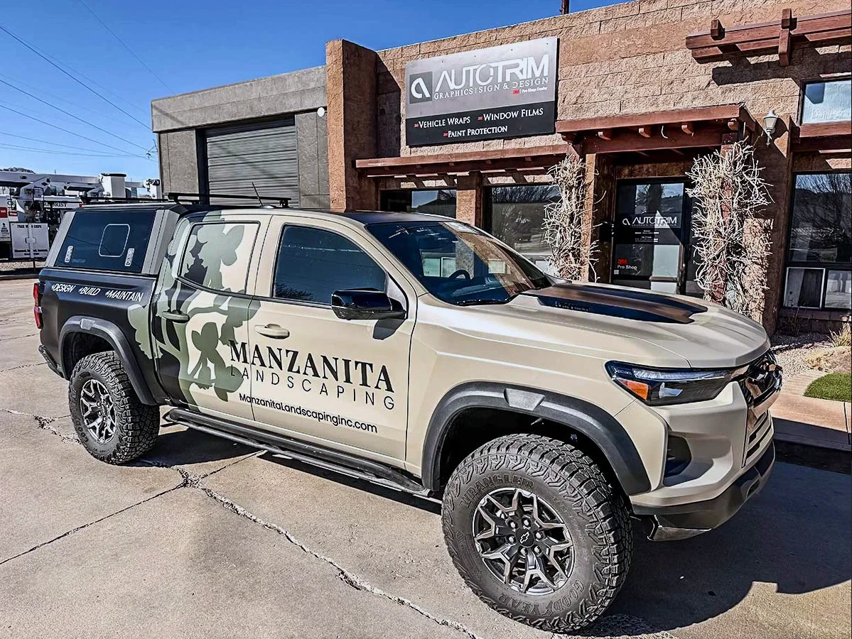 A Manzanita Landscaping Chevrolet pickup in a tan and camo-pattern wrap outside the Auto Trim Plus shop