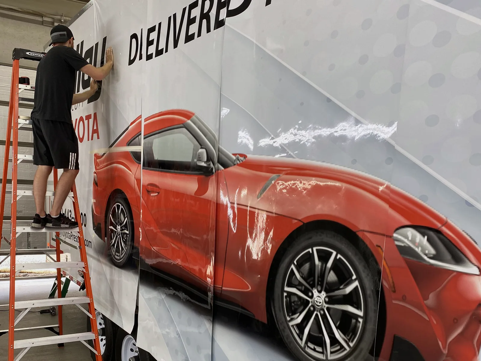 An Auto Trim Plus installer applying a full-length Toyota trailer wrap from a ladder