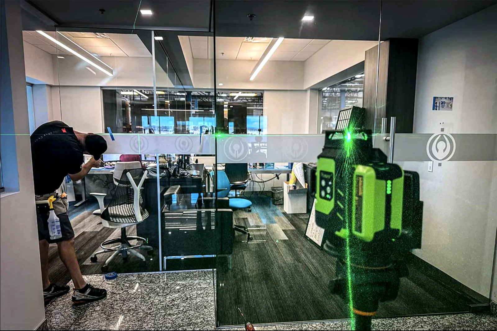Frosted film run being laser-levelled across an office glass partition