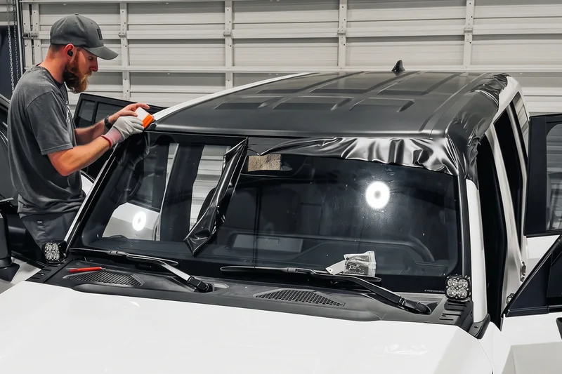 An Auto Trim Plus installer laying protection film across the Land Cruiser windshield surround